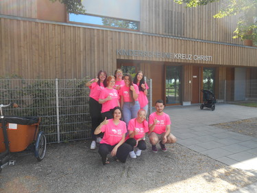 Die Gruppe des Unterkurses steht mit pinken T-Shirts vor der Kinderscheune Kreuz Christi