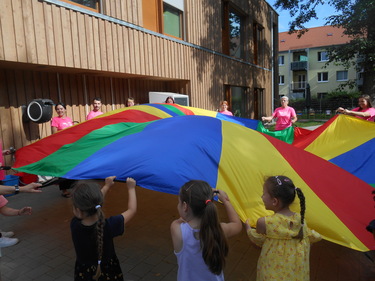 Die Kinder des Kindergartens und die Schüler:innen schwingen gemeinsam mit den Lehrerinnen das bunte Schwungtuch.