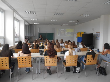 Die Klasse sitzt im Klassenzimmer an den Tischen und blickt zur Tafel, um dem Vortrag über die Ausbildung zu folgen.